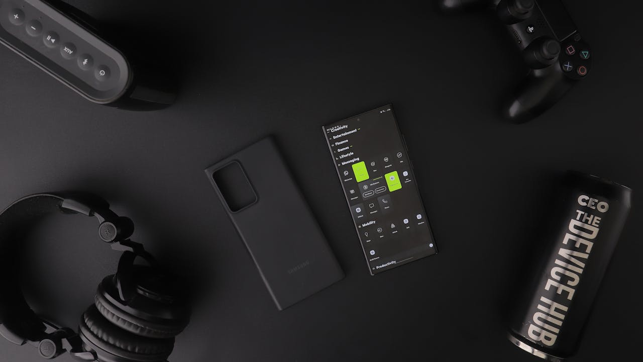 Overhead view of black modern electronics including smartphone, headphones, speaker, and controller on a table.